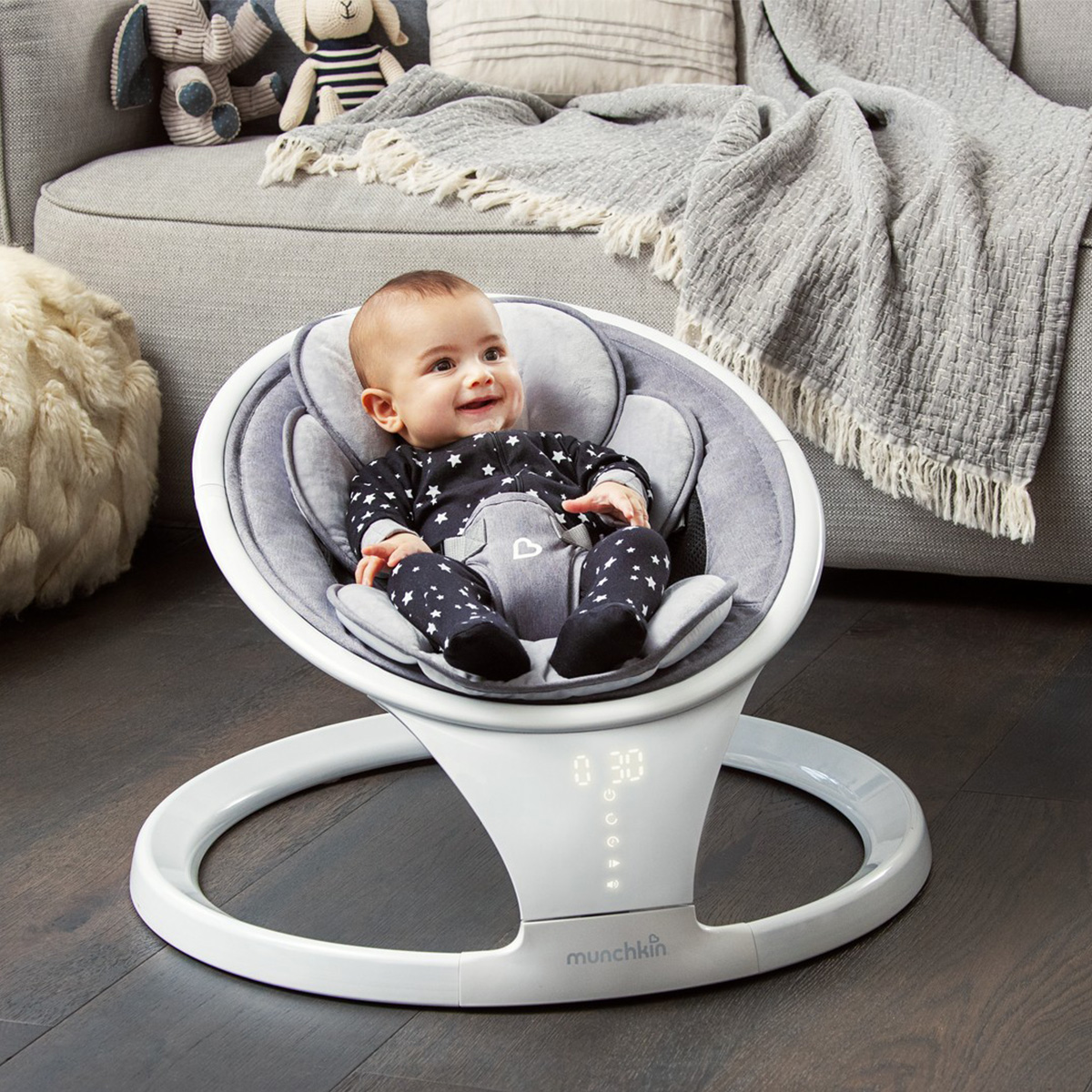A baby in a Munchkin Baby Swing with a mom looking on