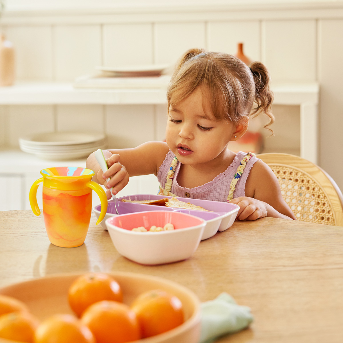 A baby with a spoon in its mouth, sitting in a high chair eating food