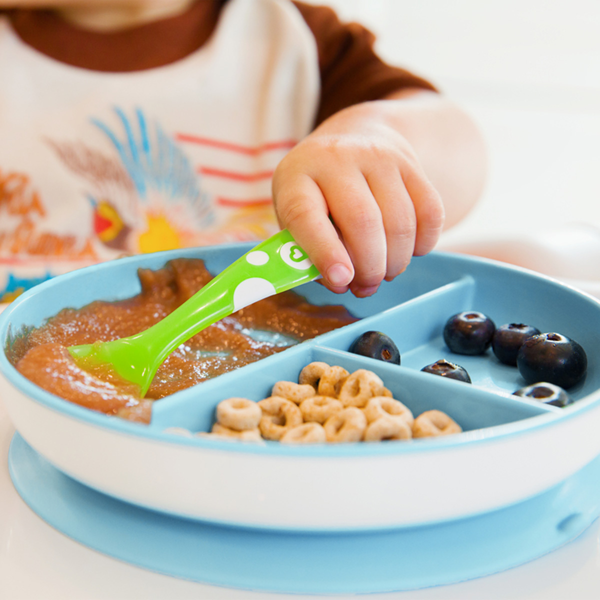 A baby spooning food with a Munchkin spoon