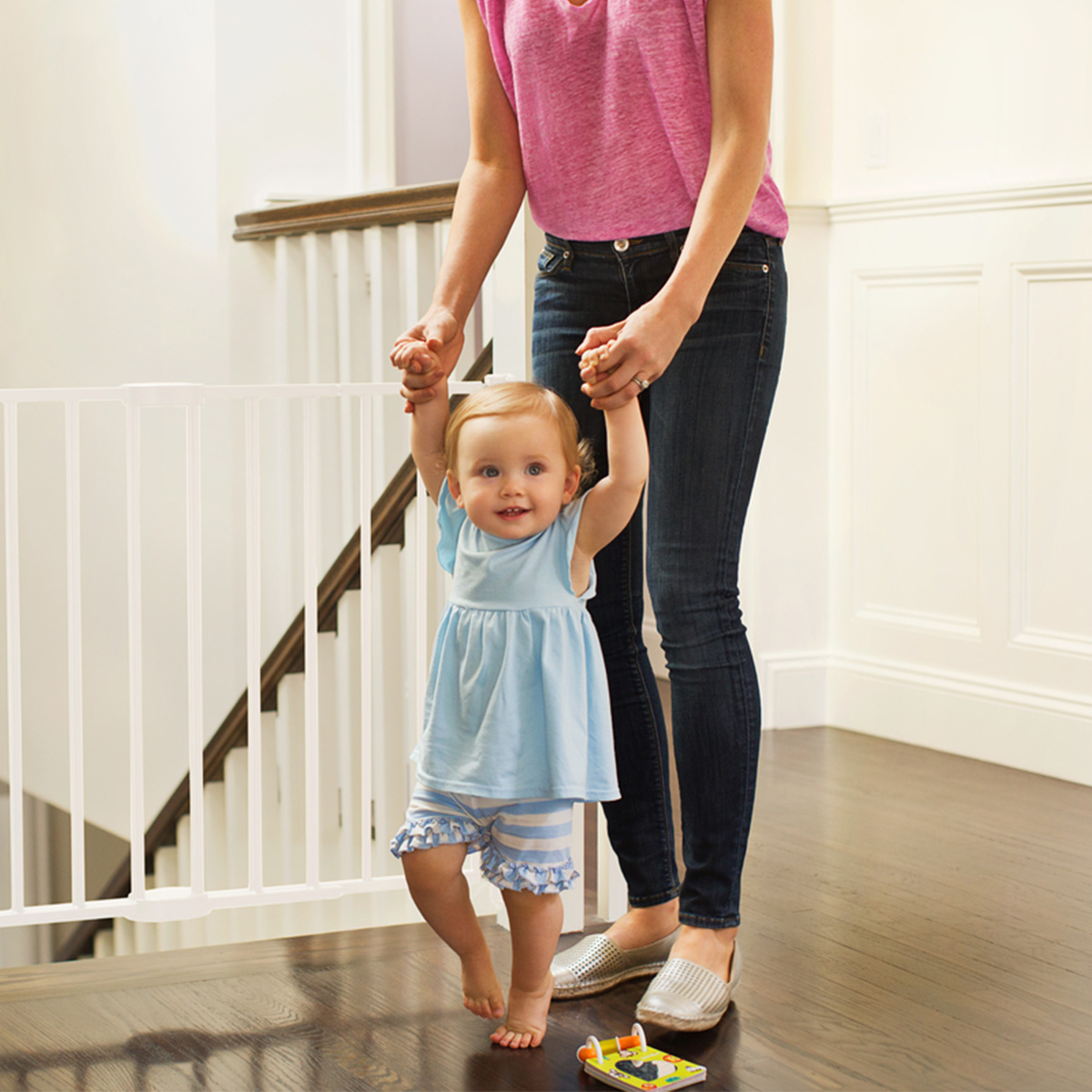 A smiley baby walking with moms help in front of a Munchkin baby gate